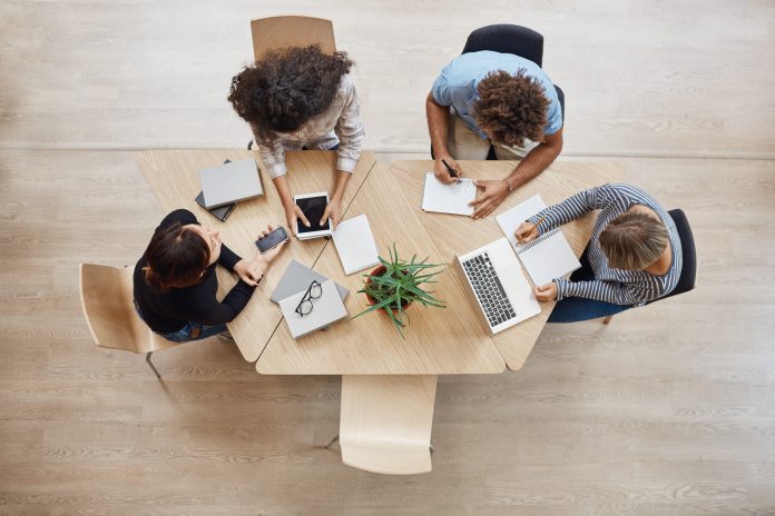 View from above. Business,startup, teamwork concept. Startup partners sitting at coworking space talking about future project, looking through examples of work on laptop and digital tablet.